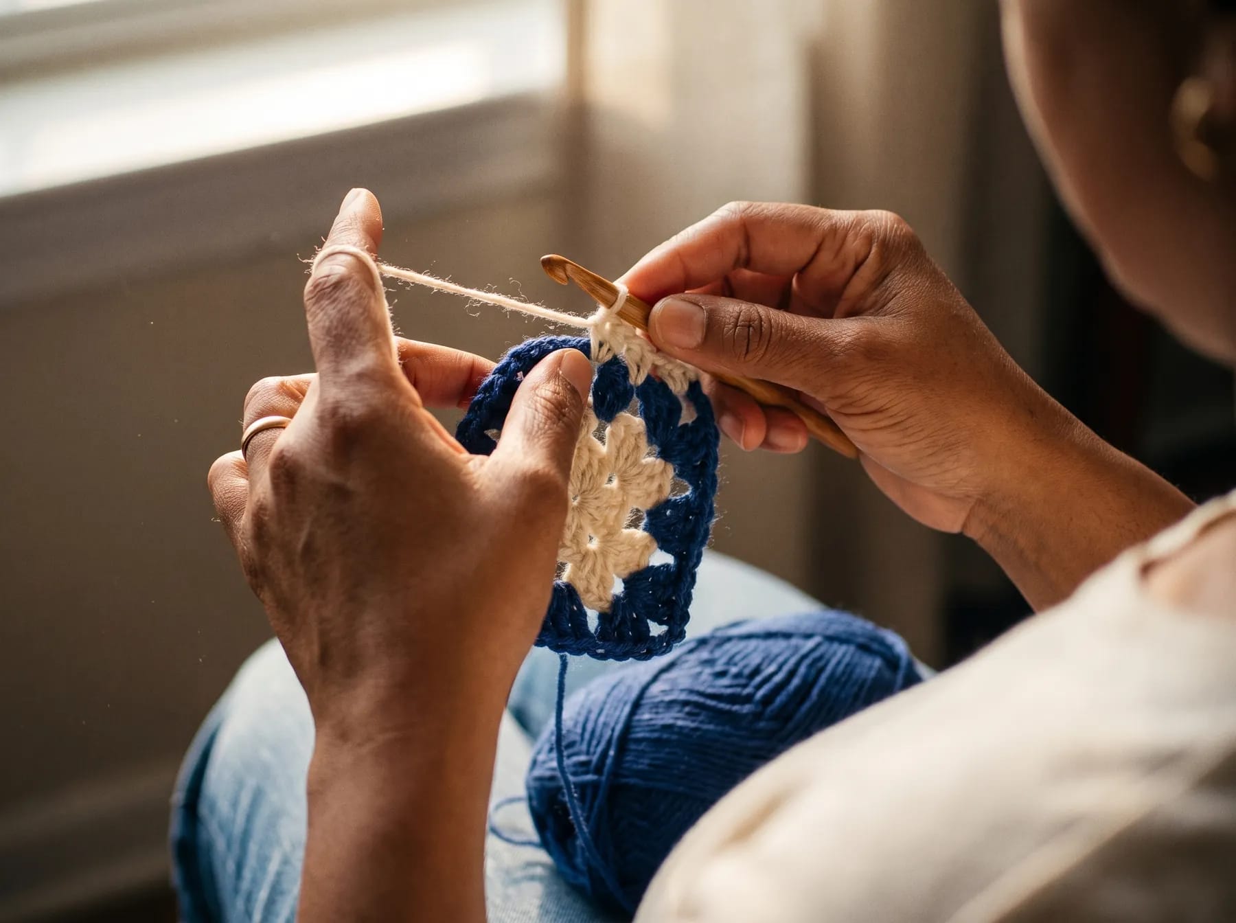 Close-up of hands crocheting a granny square with a wooden hook